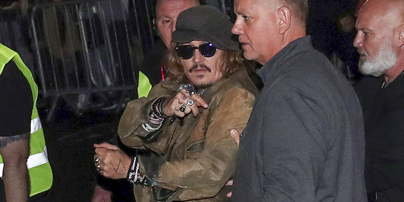 I mitten av bilden ser vi Johnny Depp i brun läderjacka, grå keps och solglasögon, han förs undan av livvakter och pekar in mot kameran.